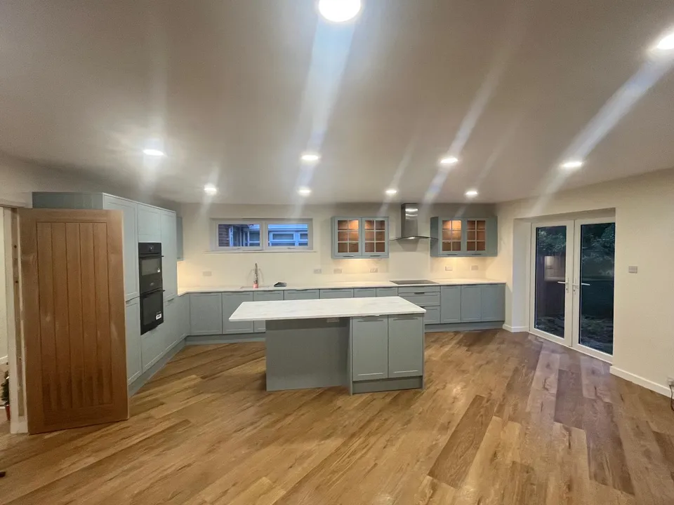 Sage-green kitchen with island, wooden floor and glazed doors