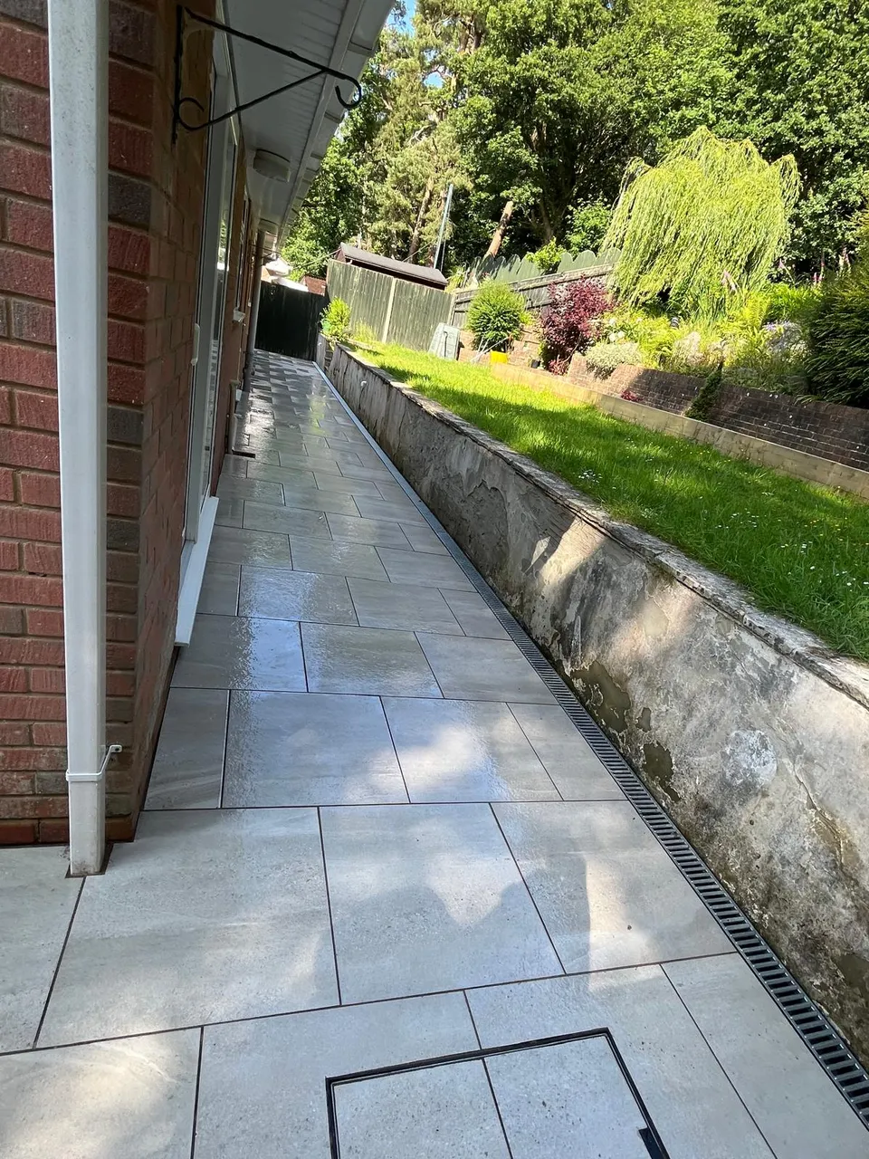 Long porcelain-paved side path with a drainage channel beside a lawn