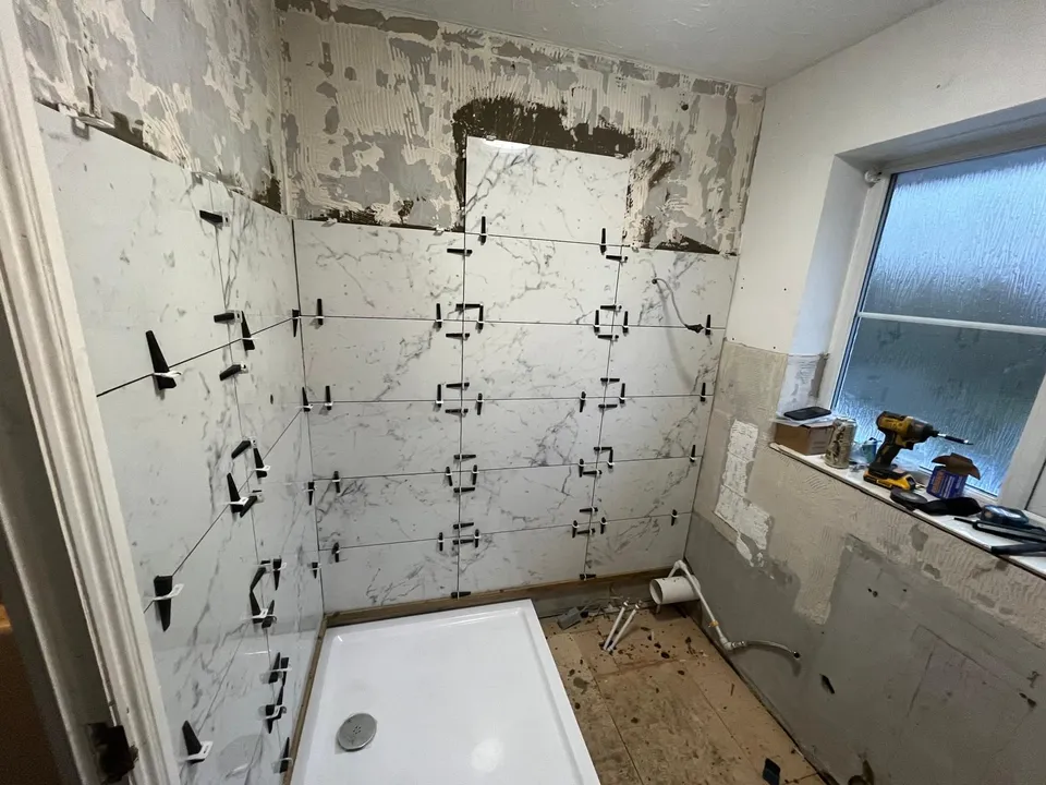Shower area mid-renovation, with large marble-effect wall tiles being fitted above a new shower tray