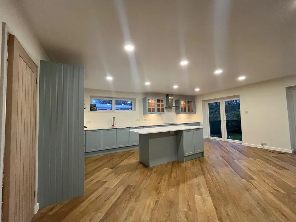 Open-plan kitchen with sage-green units seen past an oak internal door