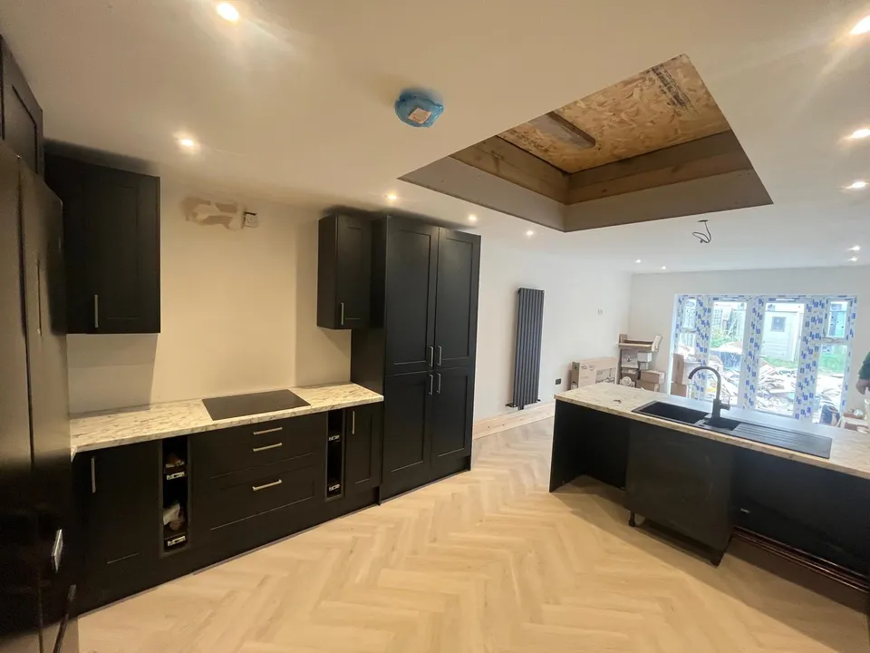Dark kitchen units and marble-effect worktops with garden doors beyond